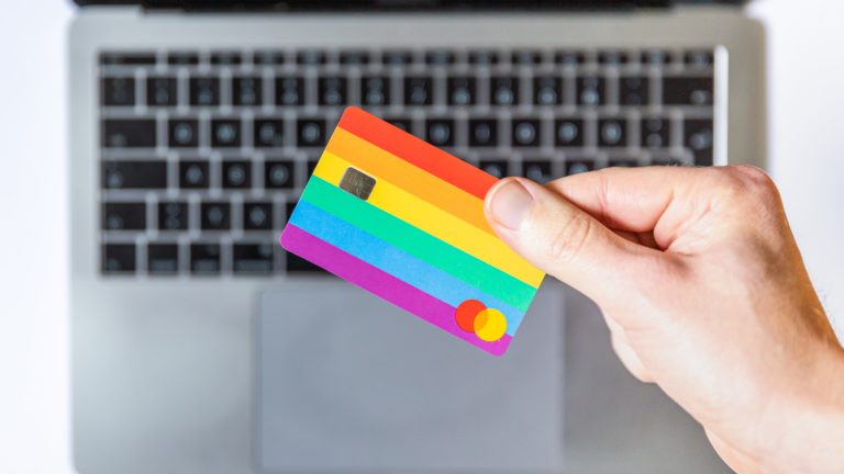 A person's hand holding a colourful Mastercard on top of a laptop