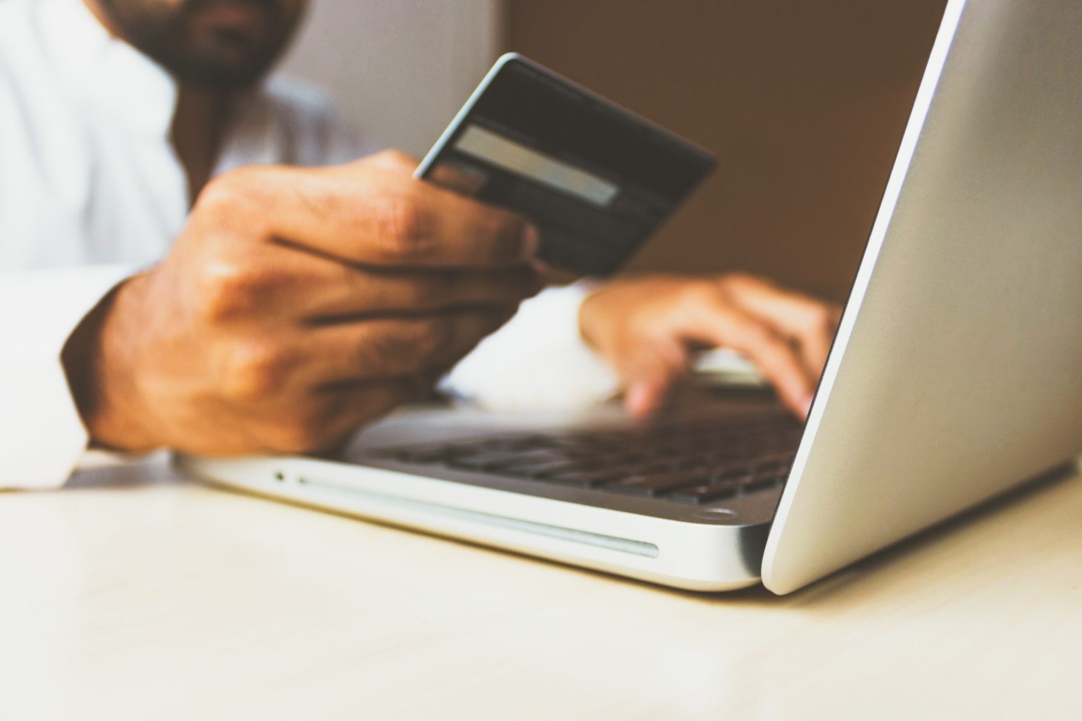 A person holding a payment card in front of a laptop performing an e-commerce transaction