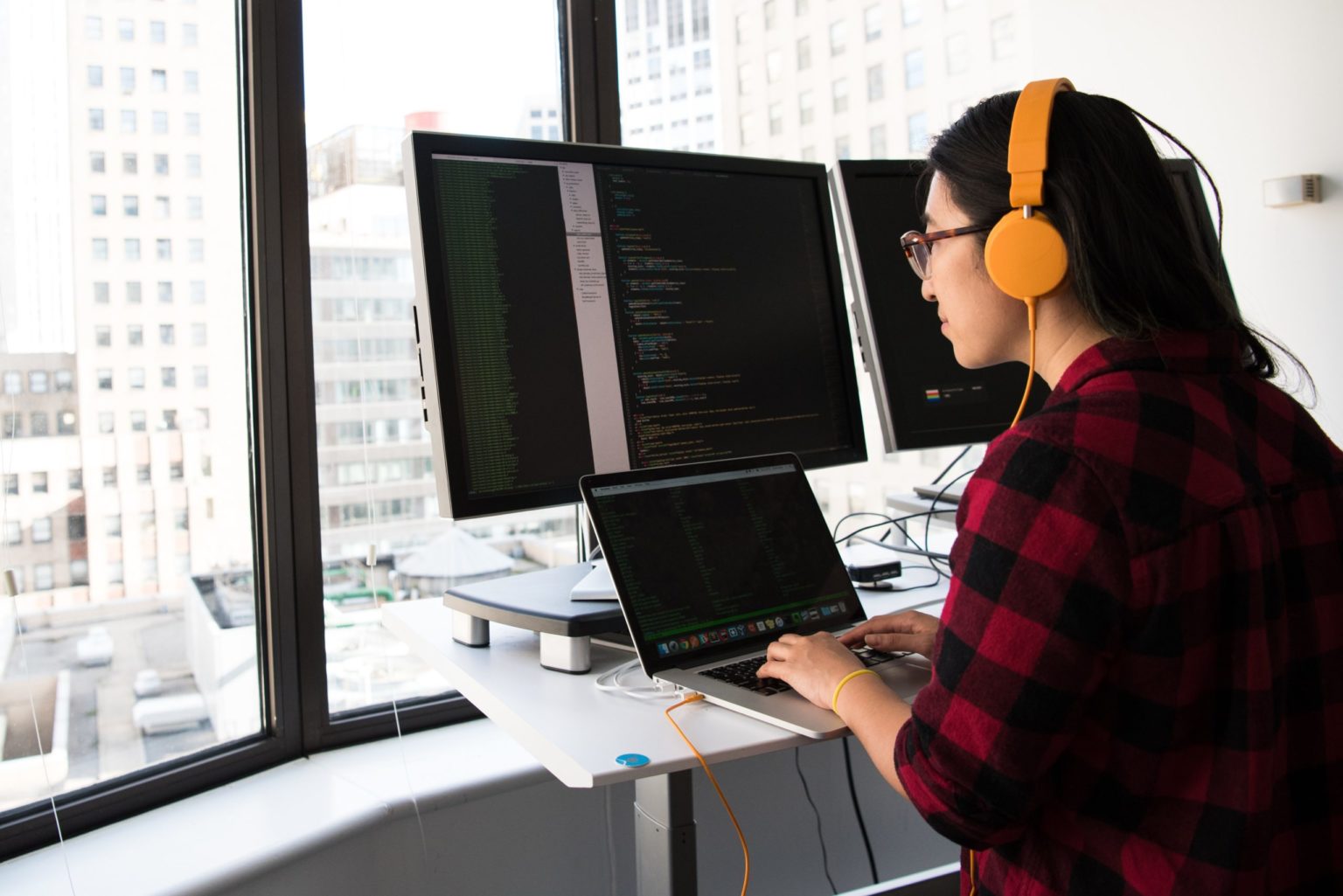 Programmer working on code on a MacBook connected to multiple monitors.