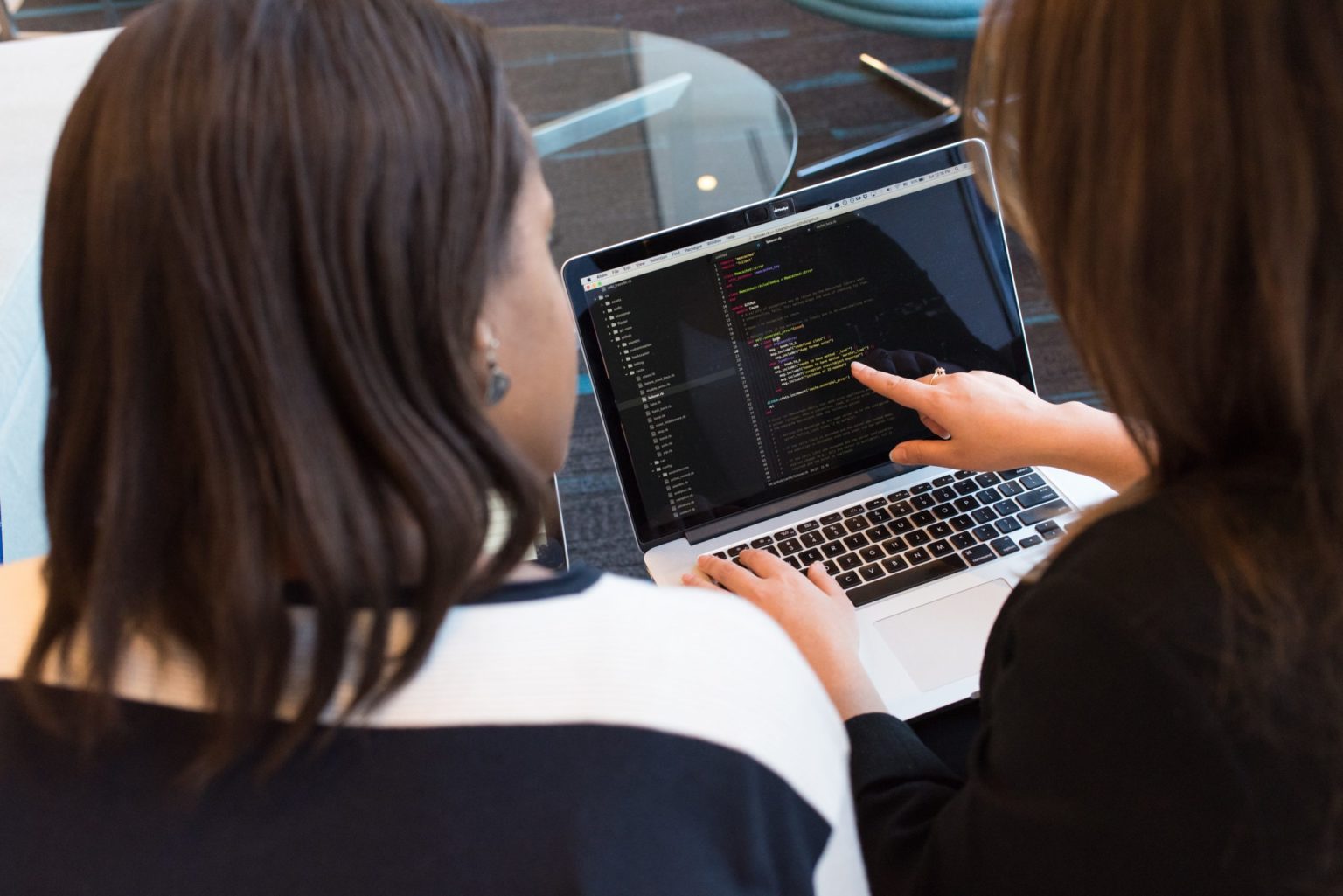 Two people discussing code displayed in a code editor on a MacBook.